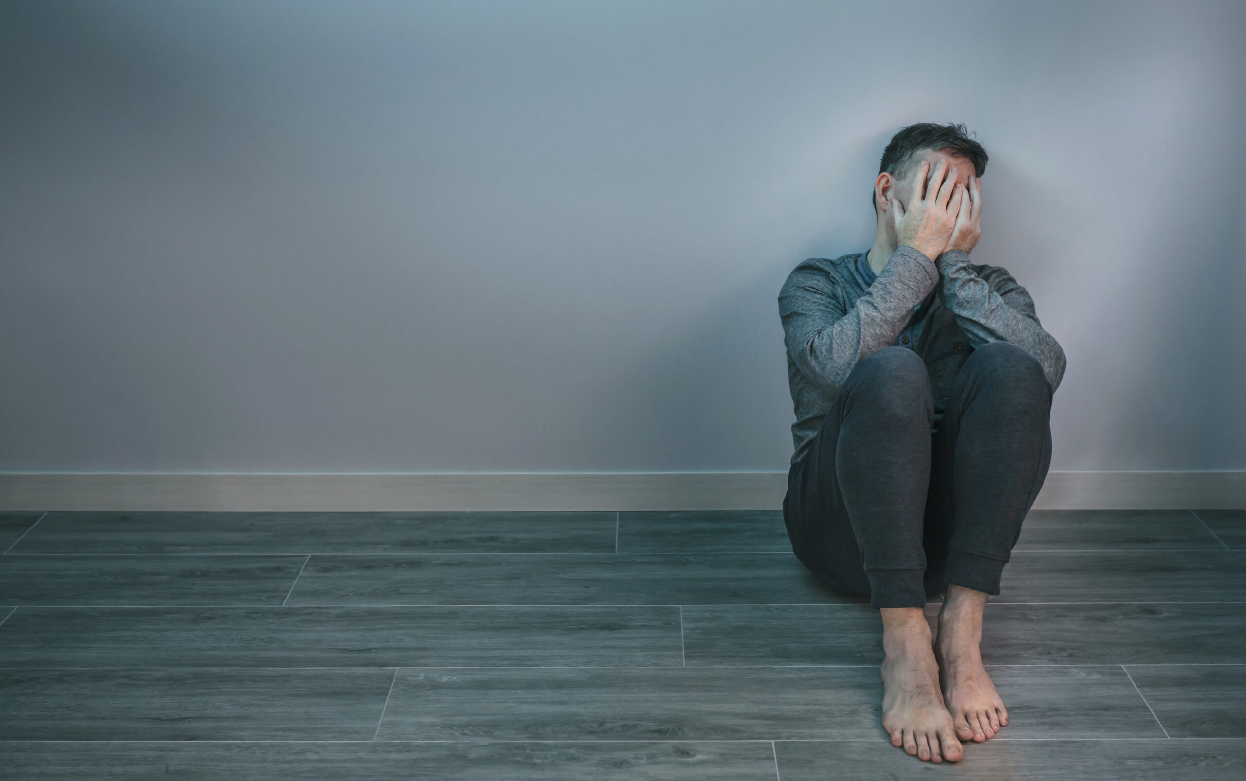 Man crying while covering his face with hands sitting on the floor bipolar and addiction treatment