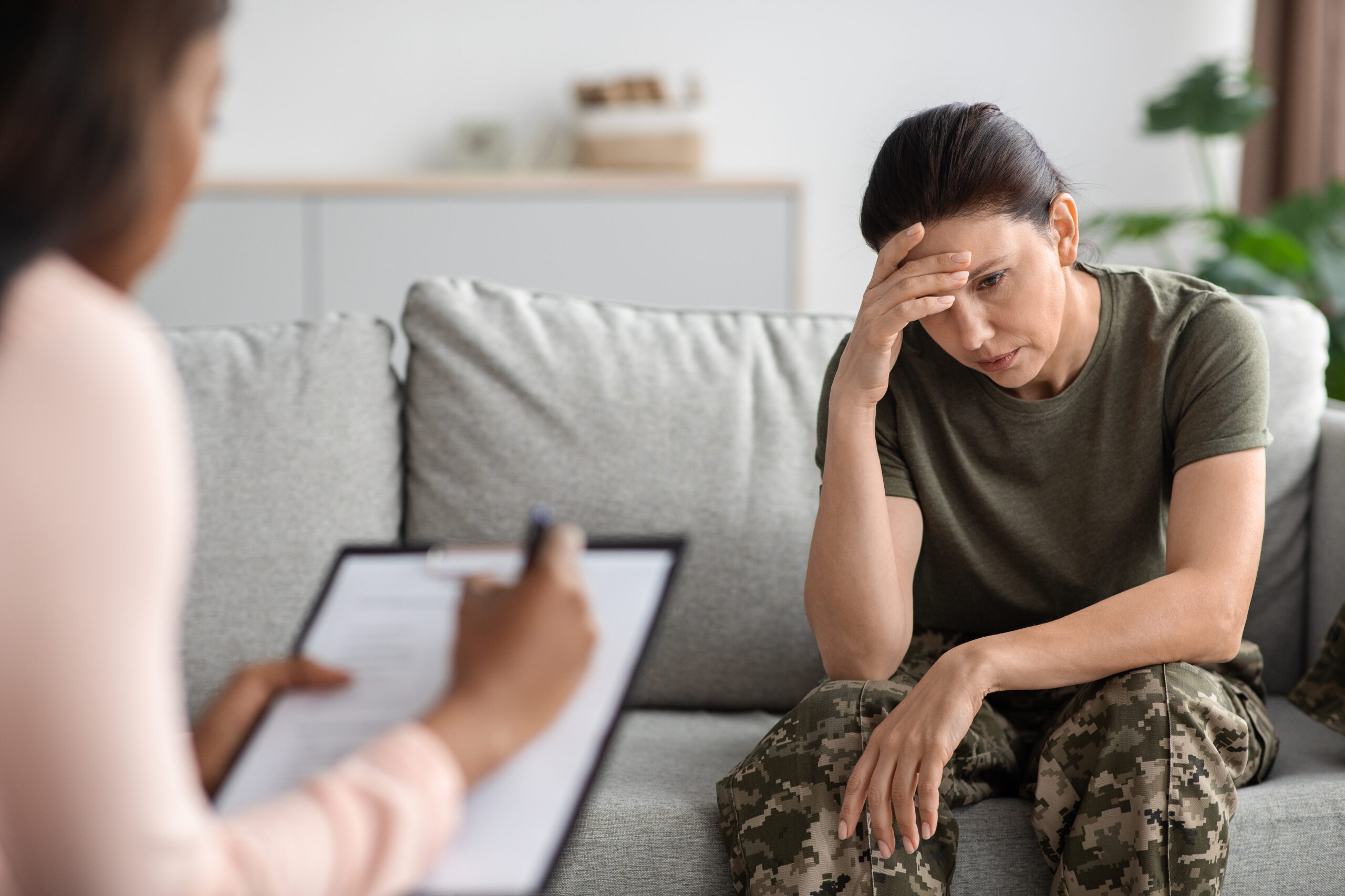 Military psychiatry concept. Depressed soldier lady sitting on couch during therapy session